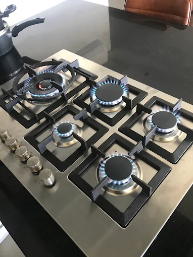 Cooktop de embutir em inox com cinco bocas acesas em chama azul e botões laterais